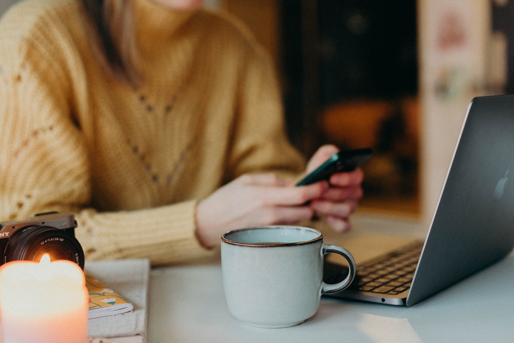 Kvinna med smarttelefon i handen och en laptop samt kaffekopp framför sig